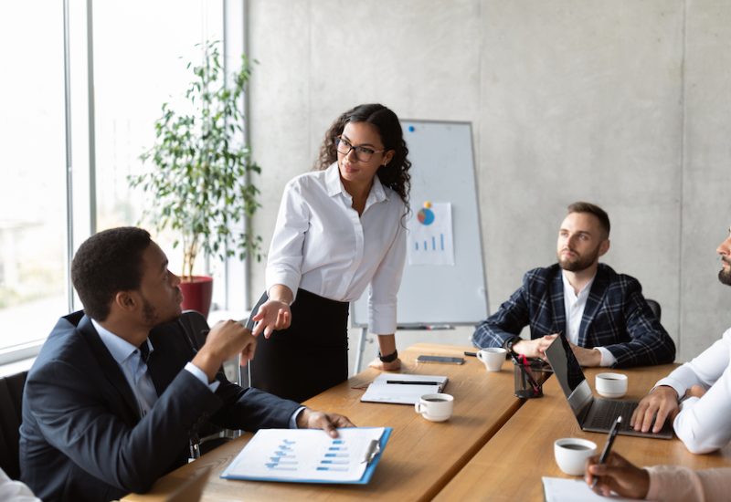 Businesswoman Giving Speech On Business Meeting With Colleagues, Discussing Work Ideas And Projects, Making Presentation Standing In Modern Office. Teamwork, Entrepreneurship, Corporate Meeting